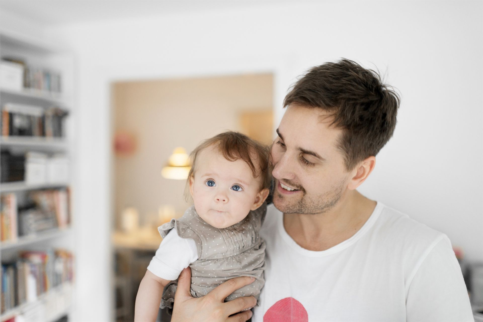En man håller ett barn inne i en lägenhet. Mannen ser glad ut.